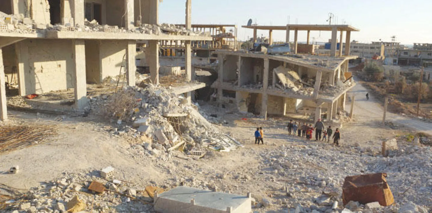 رجل مع  أطفال سوريين يسيرون بين الأنقاض في إحدى مدن محافظة درعا أمس (رويترز)