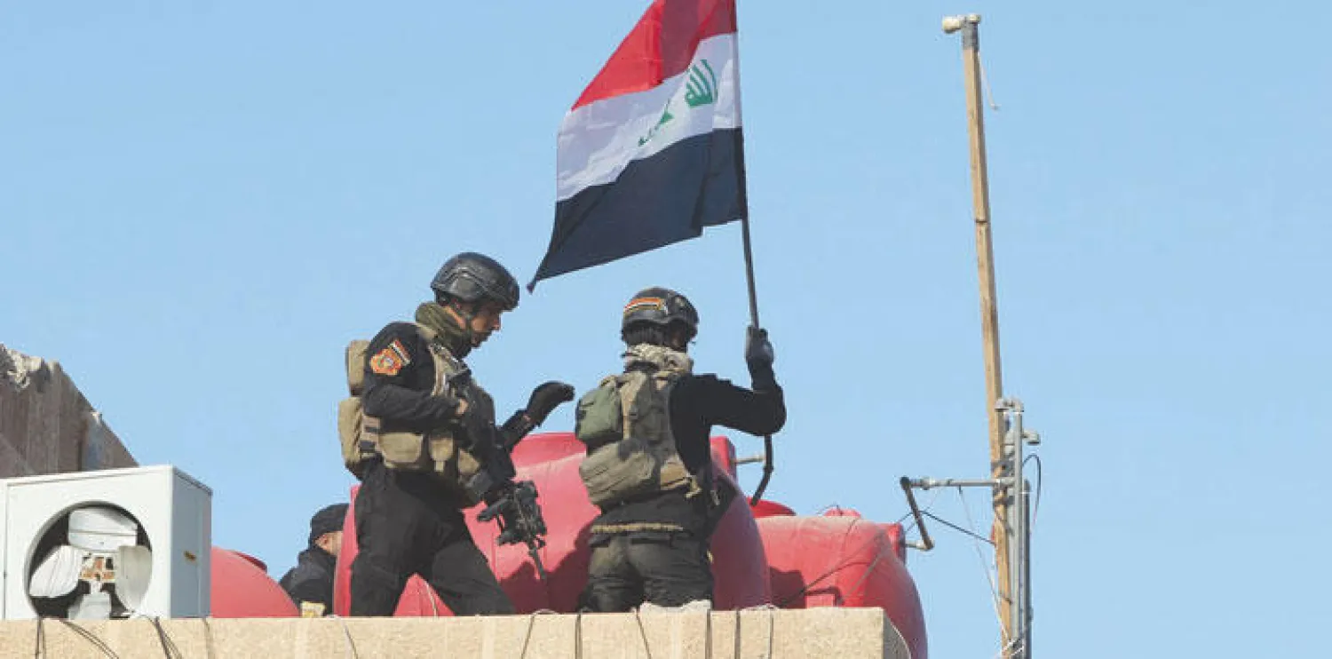 عنصران في جهاز مكافحة الإرهاب يرفعان العلم العراقي فوق مبنى داخل المجمع الحكومي في الرمادي أمس (أ.ف.ب)