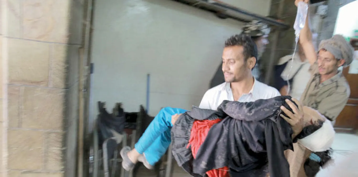 يمني يحمل طفلة أصيبت بسبب القصف الحوثي على مدينة تعز (رويترز)
