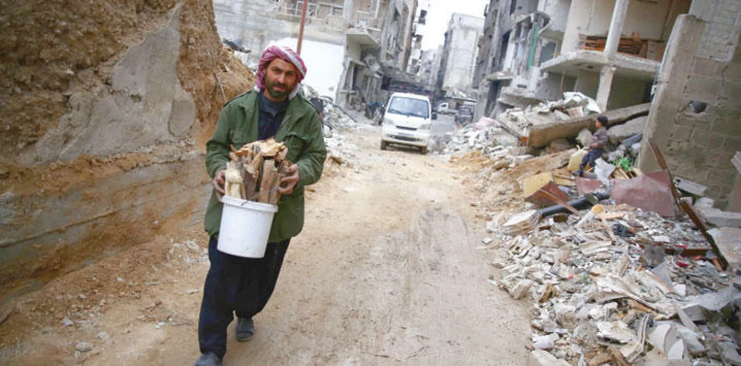 رجل من بلدة دوما بريف دمشق يجمع الخشب من ركام الأبنية المدمرة للتدفئة في ظل شح مواد الوقود (أ.ف.ب)