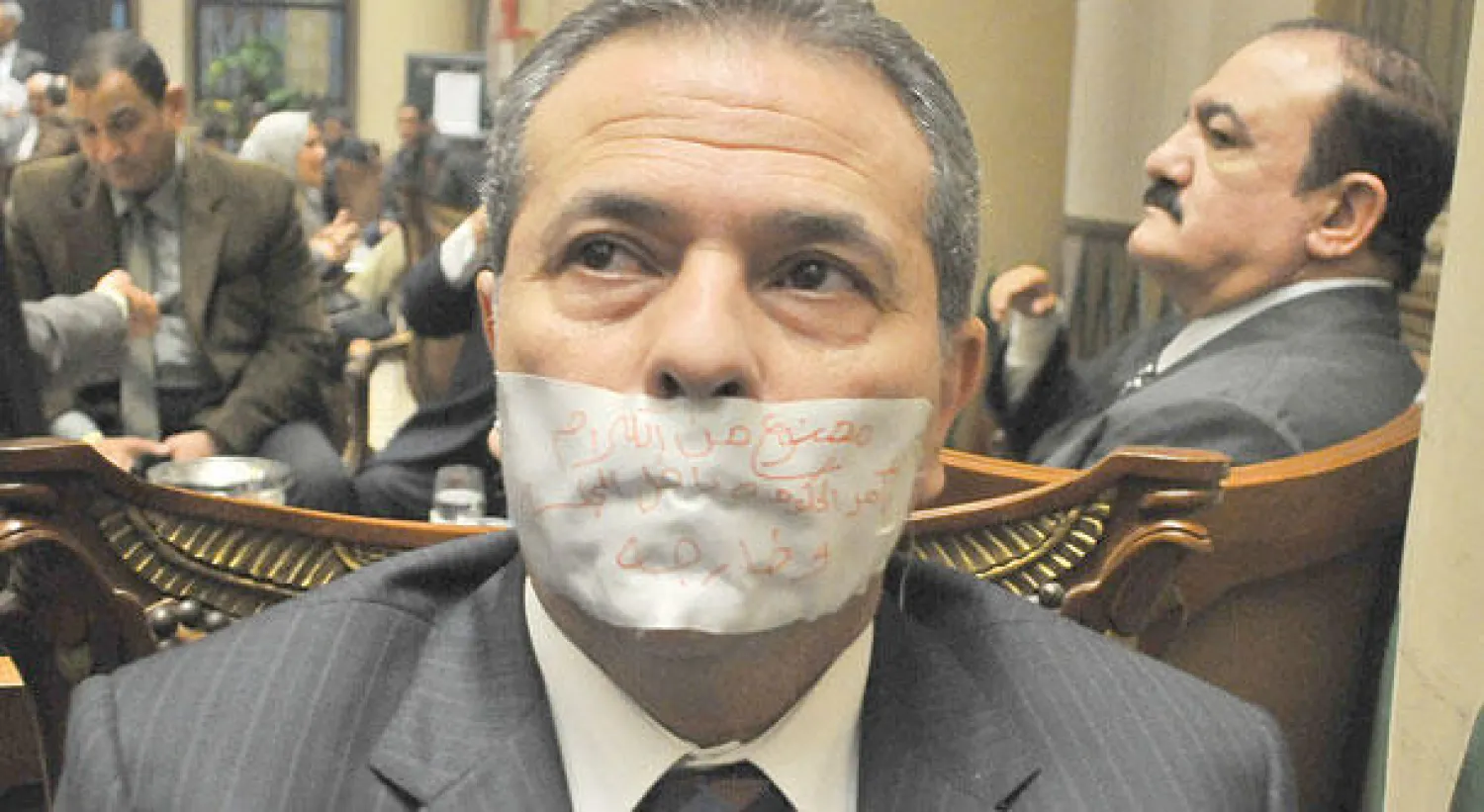 النائب توفيق عكاشة مكمما وقد كتب على الكمامة «ممنوع من الكلام بأمر الحكومة داخل المجلس وخارجه» ({الشرق الأوسط})