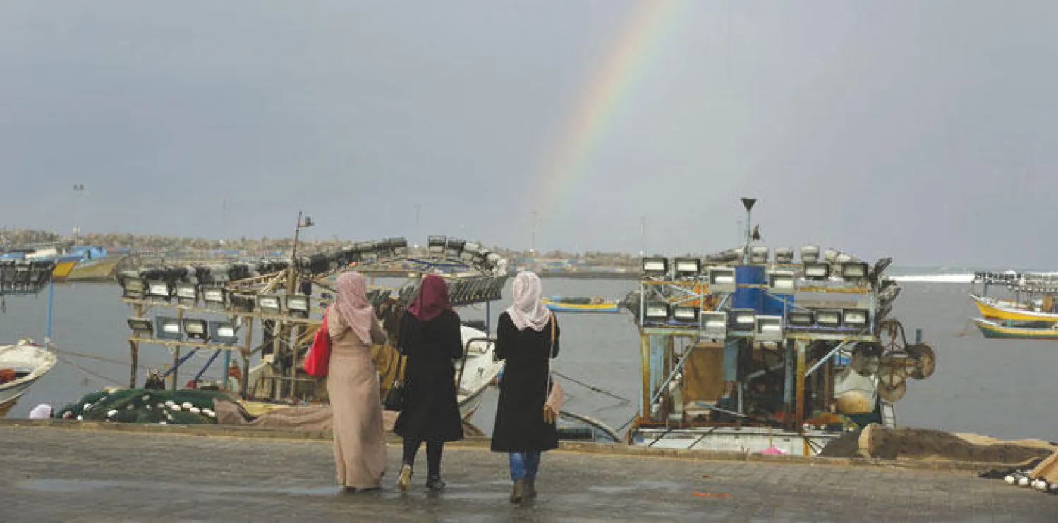 فلسطينيات يتمشين على شاطئ البحر ويشاهدن قوس قزح في سماء غزة (أ.ف.ب)