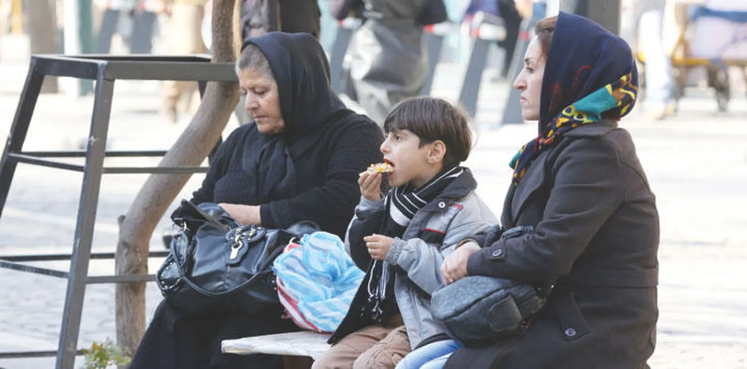 أفراد أسرة إيرانية يجلسون خارج البازار الكبير في طهران (أ.ف.ب)