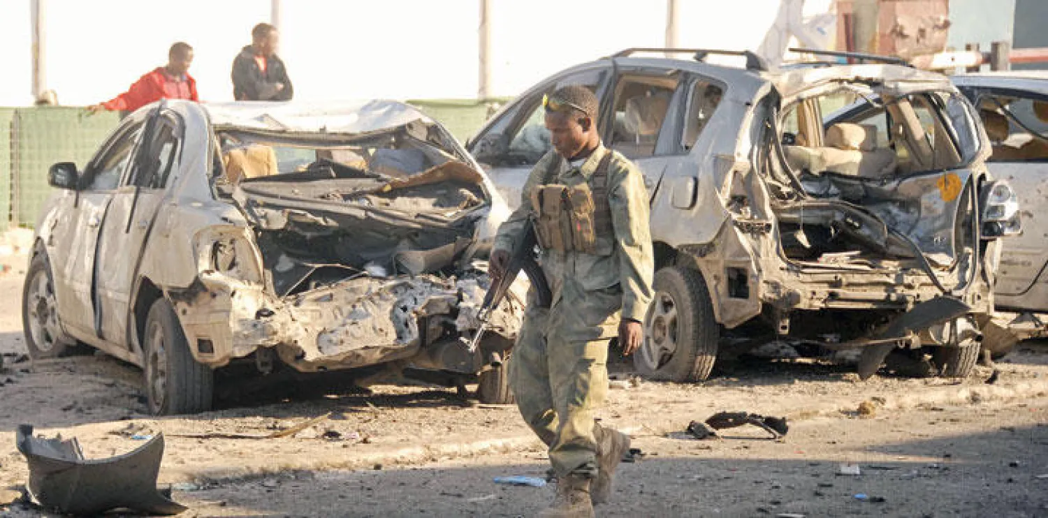 جندي صومالي يمر أمام سيارات محطمة بفعل التفجير الإرهابي أمام مطعم ليدو في العاصمة مقديشو أمس (أ.ف.ب)