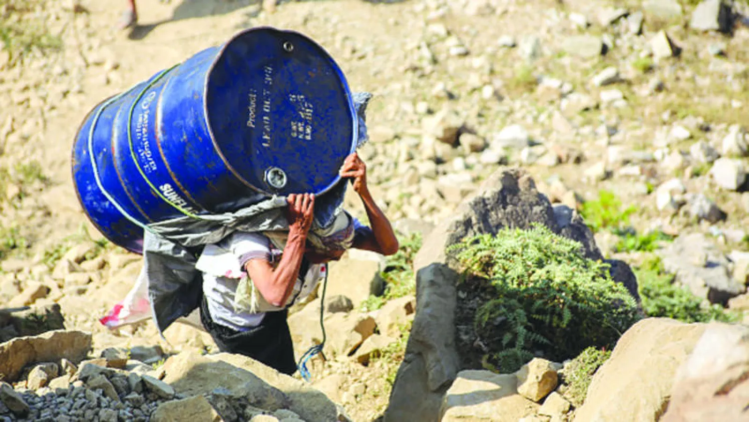 رجل يمني يحمل برميلا وسط  الجبال على طول الطريق الوحيد الذي يربط بين مدينتي عدن وتعز في محاولة لتجنب حظر الطرق الرئيسية المؤدية إلى المدينة المحاصرة من الميليشيات (غيتي)