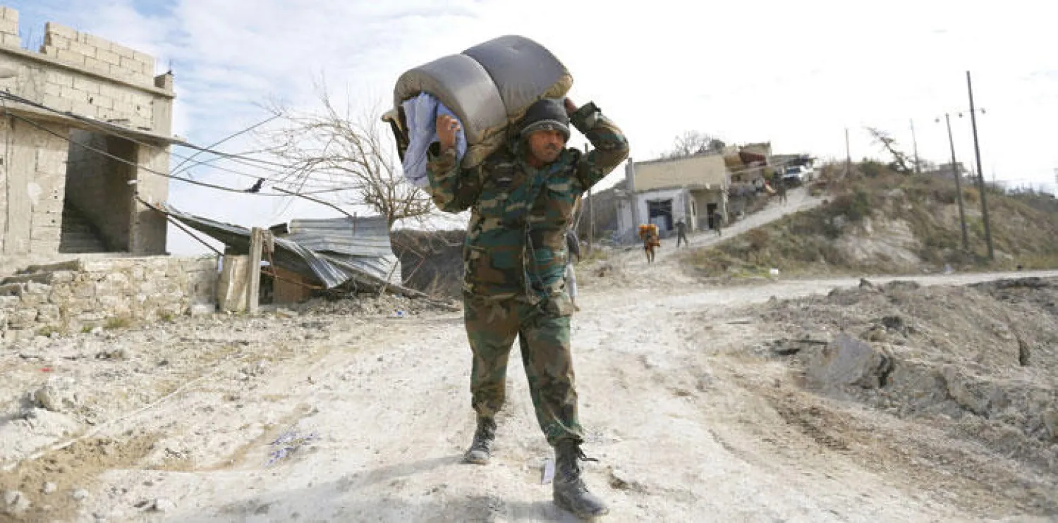 عنصر من قوات النظام السوري يحمل أغراضا استولى عليها من البيوت المدمرة والمهجورة في بلدة ربيعة التي احتلتها هذه القوات والميليشيات في شرق محافظة اللاذقية (رويترز)