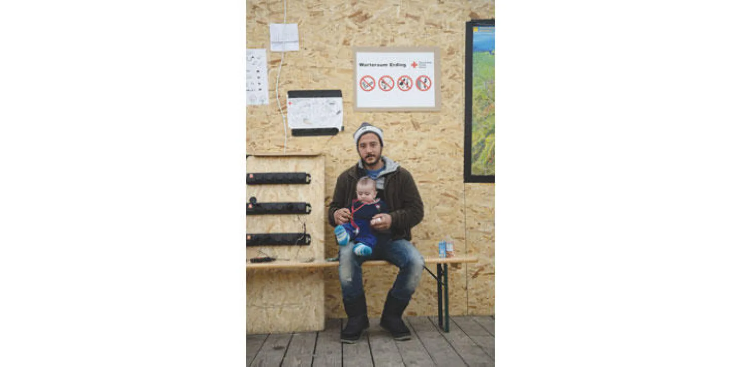 لاجئ سوري إلى ألمانيا يحمل طفله وينتظر دوره بمركز التسجيل في قاعدة اردنغ العسكرية (أ.ف.ب)