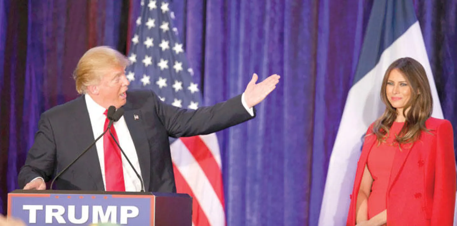 ترامب يتحدث خلال تجمع في دي موين بولاية آيوا الليلة قبل الماضية ويشير إلى زوجته ميلانيا (رويترز)