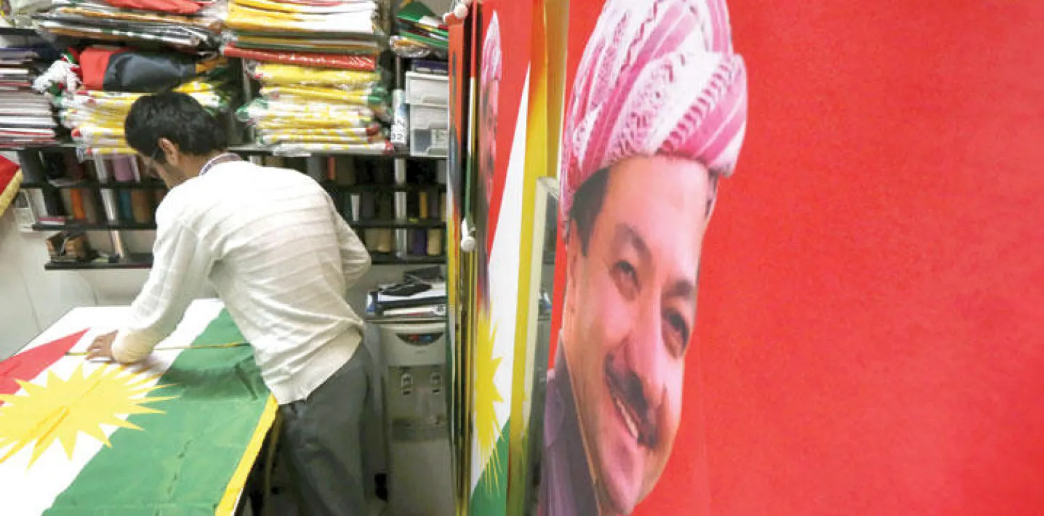 كردي عراقي يصمم علم إقليم كردستان وفيه صورة لرئيس الإقليم مسعود بارزاني (أ.ف.ب)