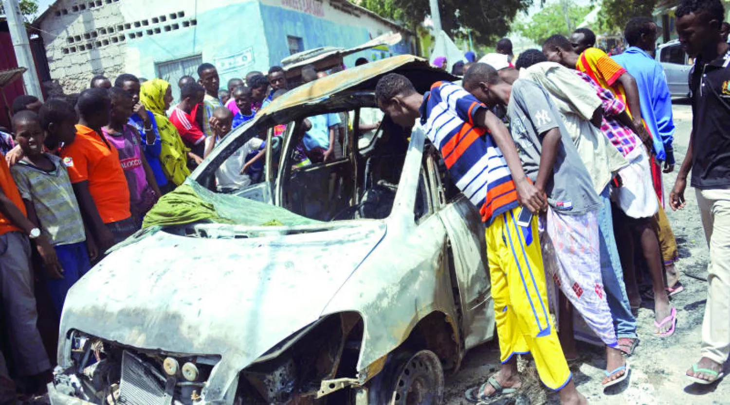 مواطنون يعاينون آثار الانفجار الذي استهدف سيارة رجل أمن في مطار مقديشو أمس (أ.ف.ب)