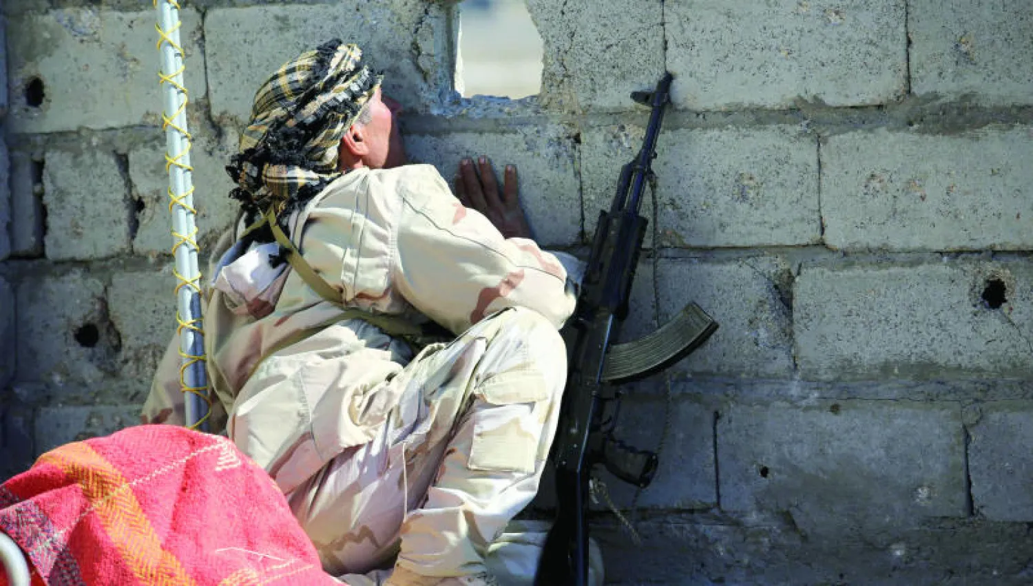 جندي عراقي ينظر من خلال فجوة في جدار غرب الفلوجة في العراق (رويترز)