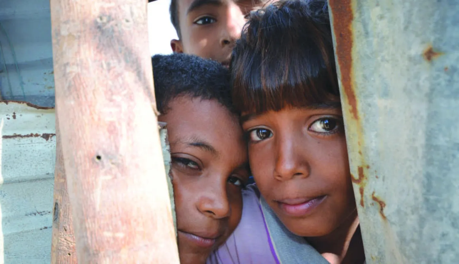 صبيان يمنيان ينظران من خلال جدار بكوخ في أحد الأحياء الفقيرة بمدينة الحديدة الساحلية المطلة على البحر الأحمر (رويترز)