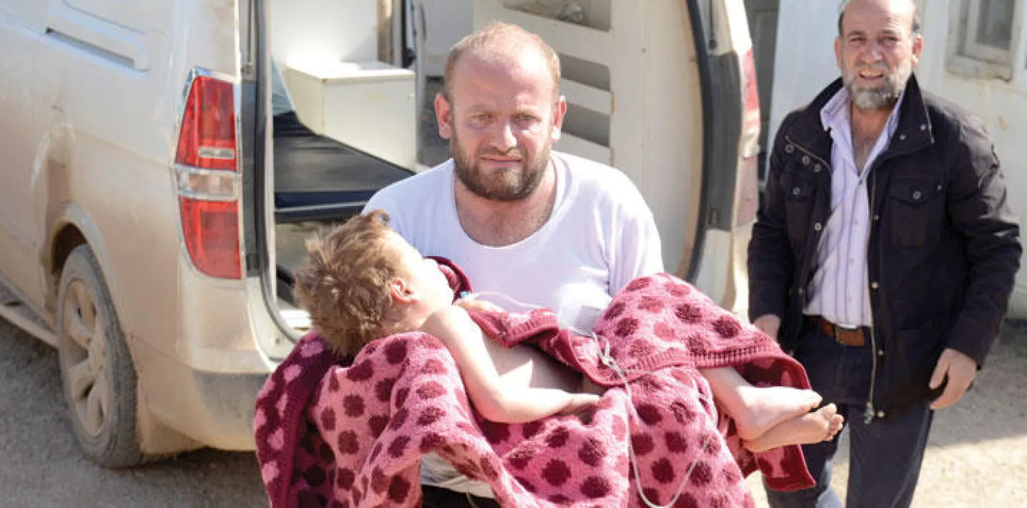 رجل من مدينة أعزار بريف حلب قرب الحدود التركية يحمل طفلة مصابة جراء هجمات جوية روسية على المنطقة أمس (غيتي)