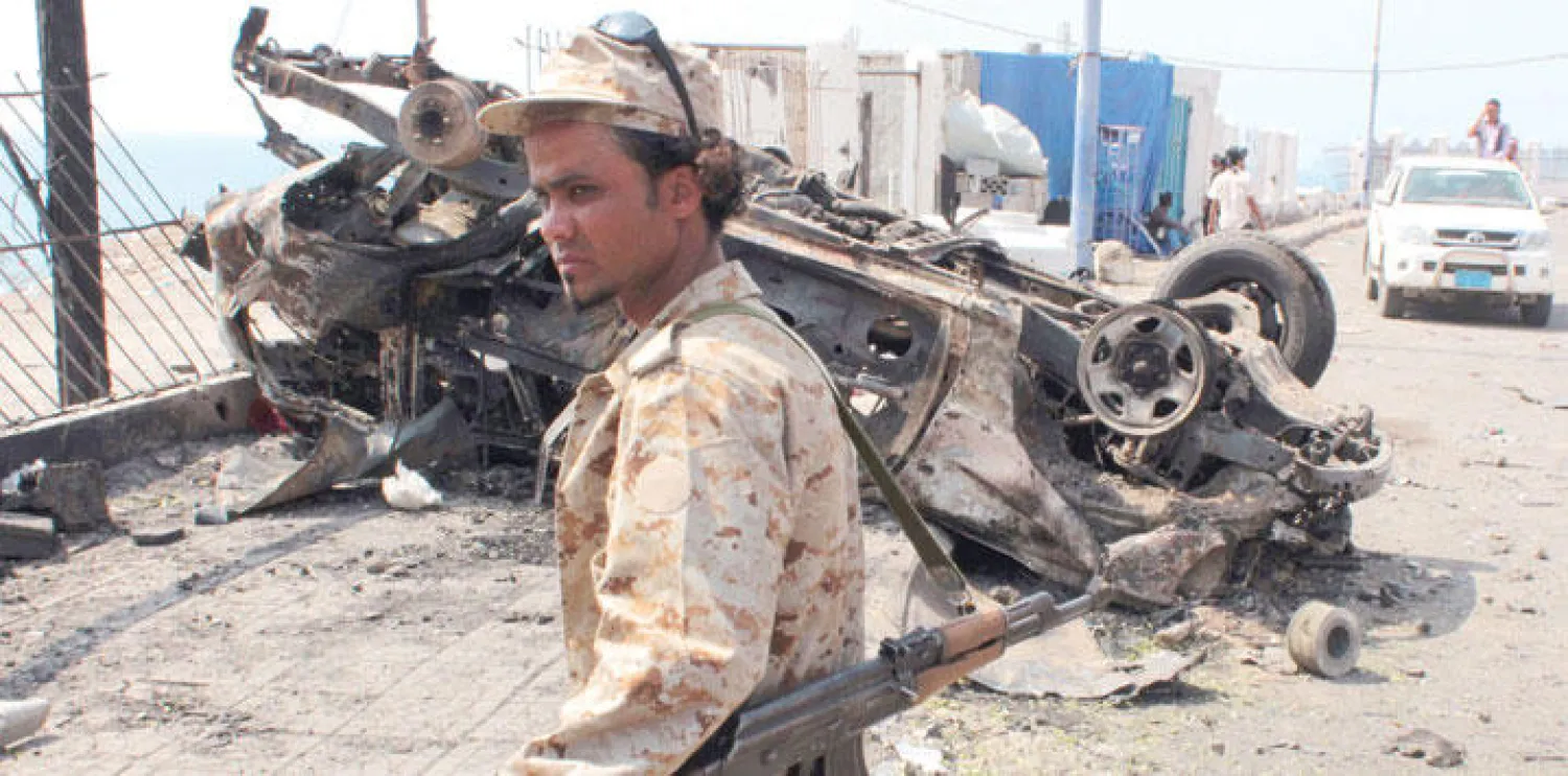 عنصر من قوات الأمن اليمنية يقف بجانب حطام  سيارة في أعقاب تفجير انتحاري طال مقرا أمنيا في عدن (أ.ف.ب)