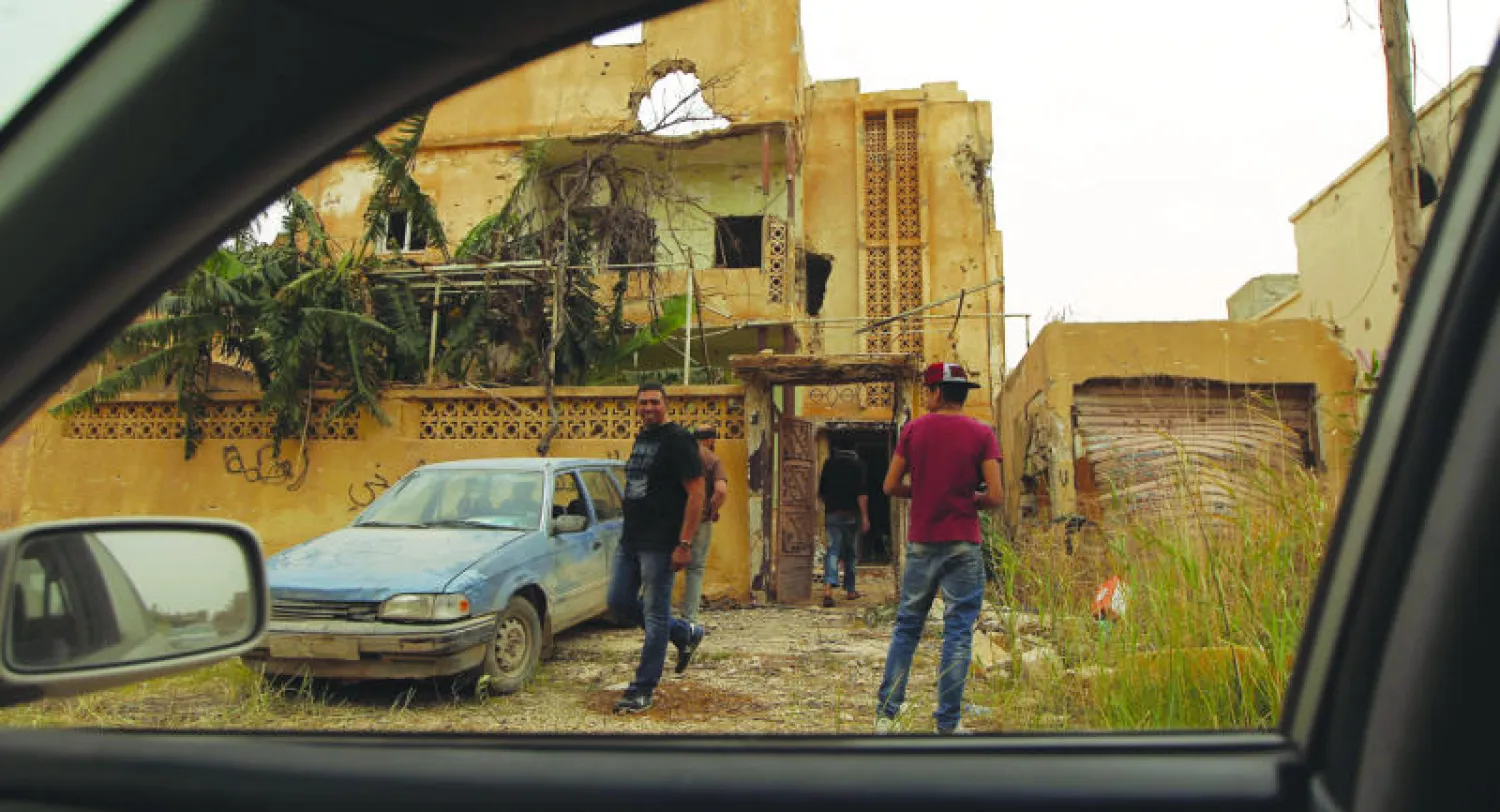صورة مأخوذة من داخل سيارة لليبيين أمام منزل متضرر بمنطقة أعادت القوات الشرعية السيطرة عليها في مدينة بنغازي أمس (أ.ف.ب)