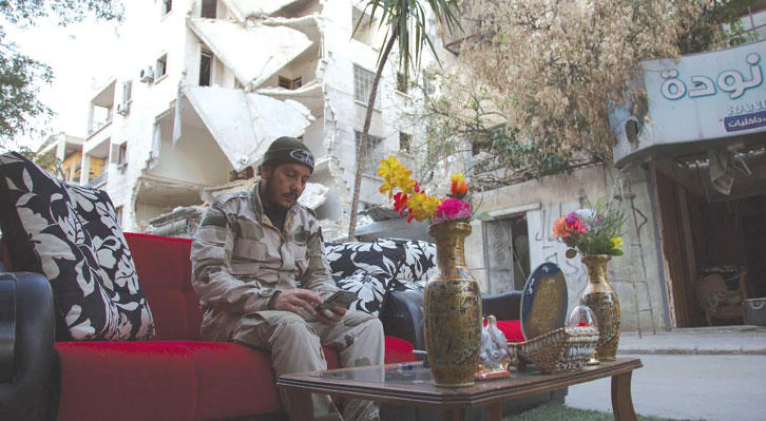 أبو نورا من الجبهة الشامية يتحدث عبر هاتفه الجوال إلى أفراد من عائلته بينما يجلس وسط منطقة دمرت بالقنابل في  حلب (أ.ف.ب)