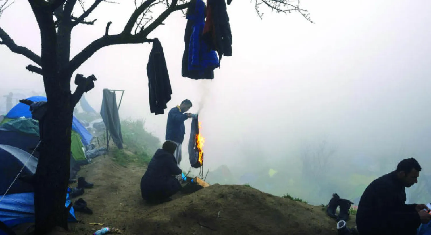 لاجئ يحرق بعضا من ثيابه للحصول على نار خلال صباح ضبابي في مخيم مؤقت على الحدود اليونانية - المقدونية حيث أغلبية اللاجئين من السوريين (أ.ف.ب)