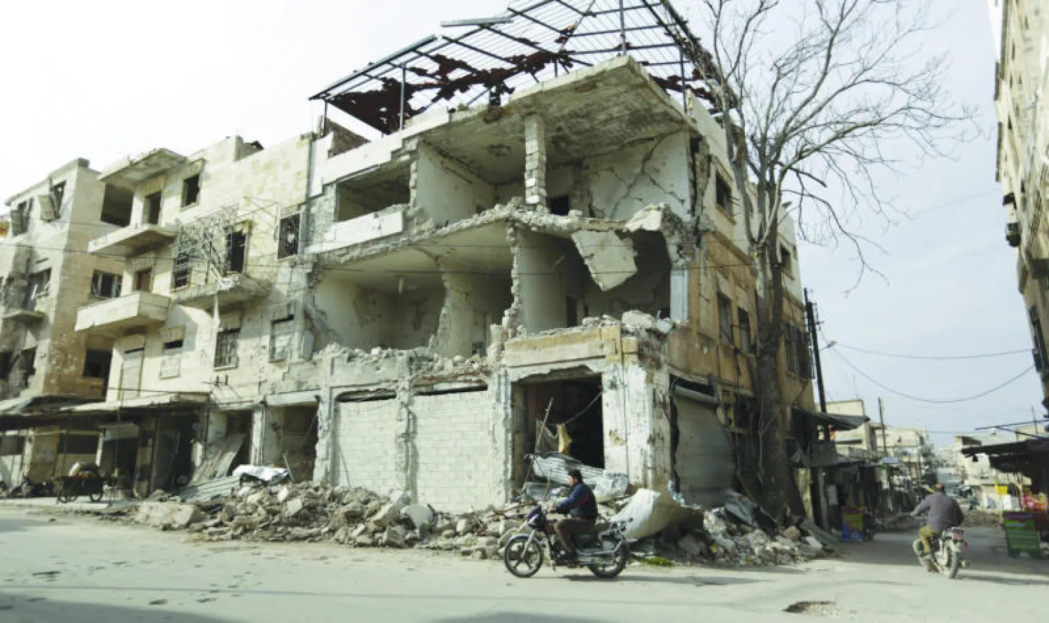 سوري يستقل دراجته النارية قرب مبنى مدمر في معرة النعمان بمحافظة إدلب أول من أمس (رويترز)