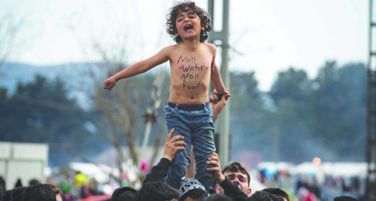 مهاجرون وطالبو لجوء يحملون طفلا في مظاهرة في أحد المخيمات القريبة من ادوميني على الحدود اليونانية - المقدونية أمس (أ.ف.ب)