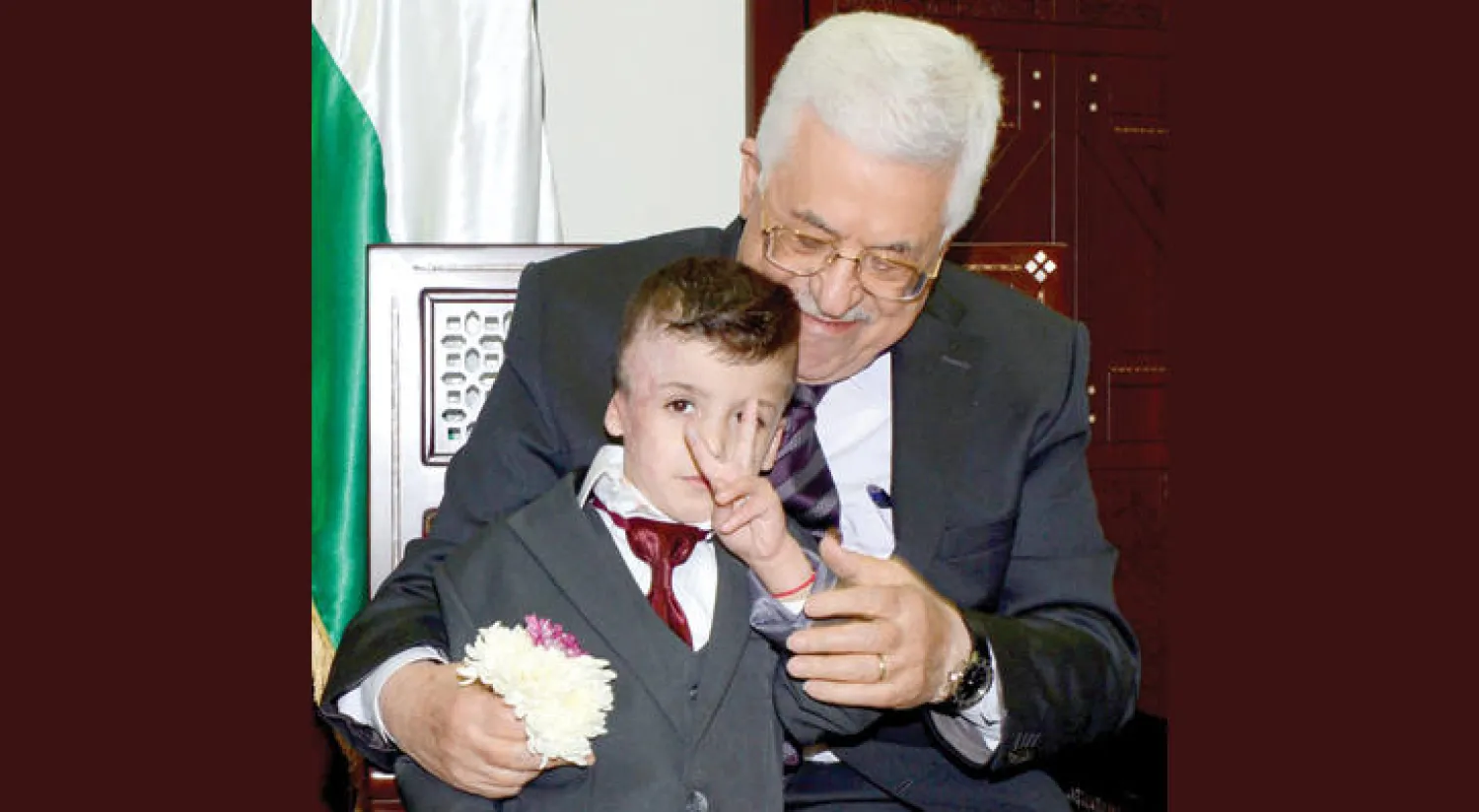 الرئيس الفلسطيني محمود عباس يداعب الطفل أحمد الدوابشة الذي نجا من حريق أشعله مستوطنون أودى بعائلته (أ.ف.ب)