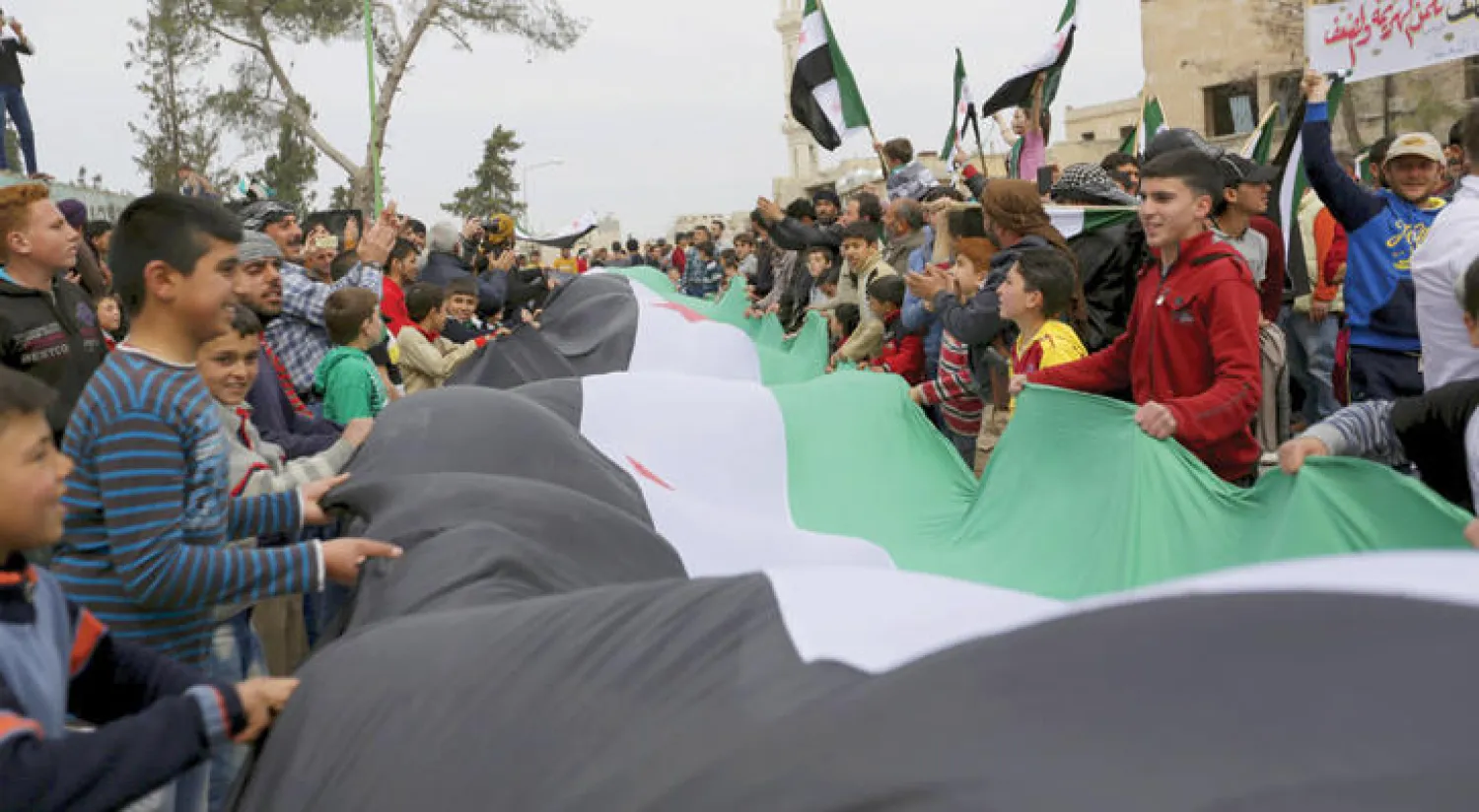 متظاهرون يحملون علم المعارضة خلال مشاركتهم في احتجاجات ضد النظام في منطقة معرة النعمان في إدلب (رويترز)