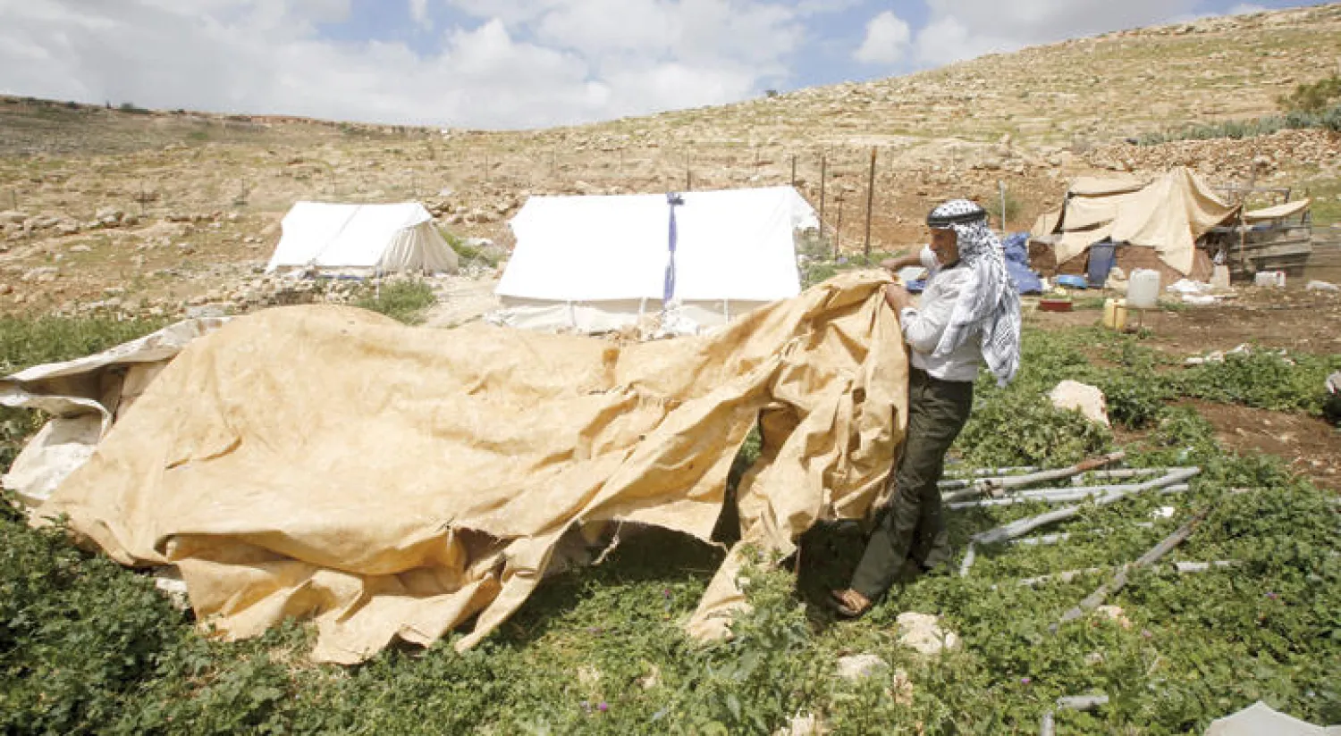فلسطيني يلملم خيمته التي أسقطتها القوات الإسرائيلية في منطقة {خربت تانا} قرب مدينة نابلس بالضفة الغربية أمس (رويترز)