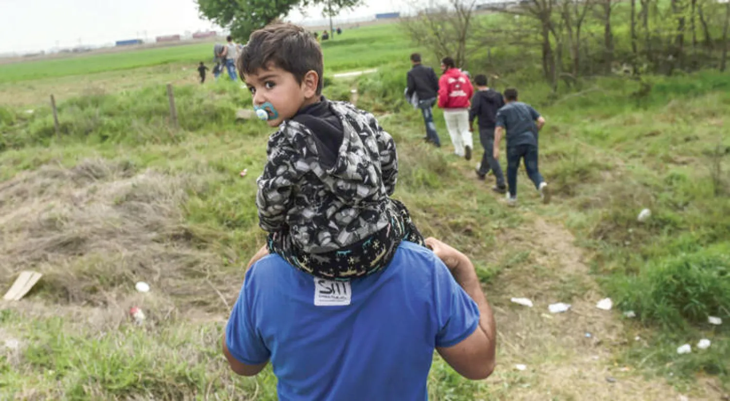لاجئ يحمل على كتفيه في طريقه مع رفقائه للتظاهر ضد غلق الحدود بين اليونان ومقدونيا أمس (أ.ف.ب)