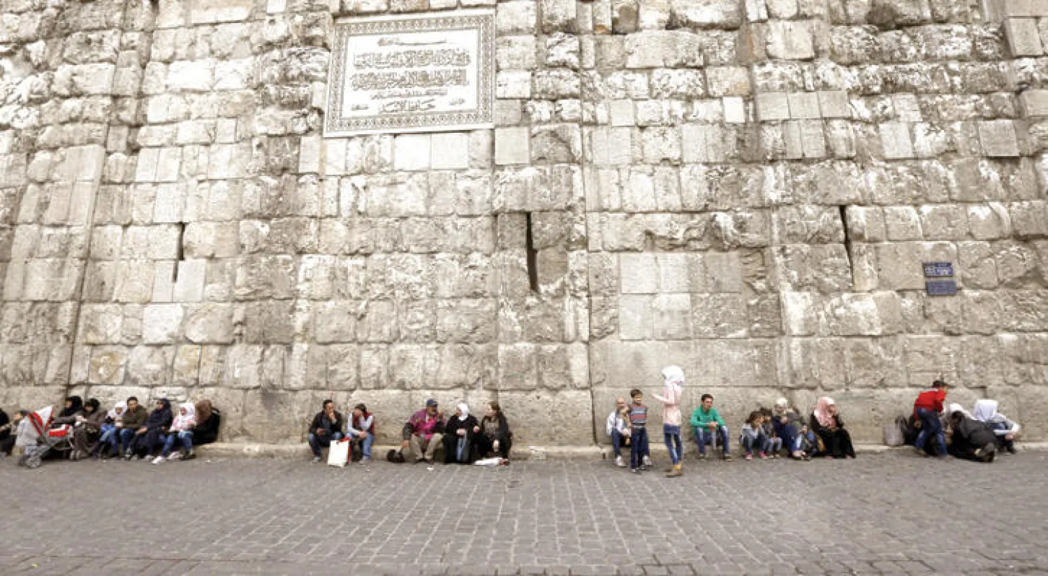 سوريون يجلسون إلى جدار الجامع الأموي في القسم القديم من العاصمة السورية دمشق (أ.ف.ب)