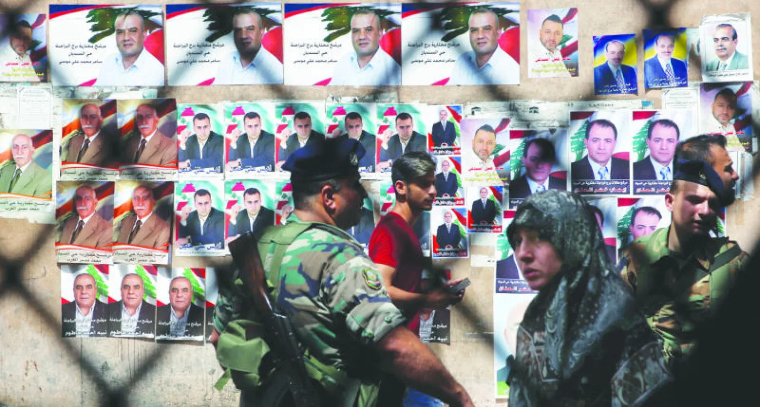 ناخبون لبنانيون ورجال أمن بالقرب من ملصقات انتخابية لمرشحي البلدية في الضاحية الجنوبية ببيروت أمس (إ.ب)