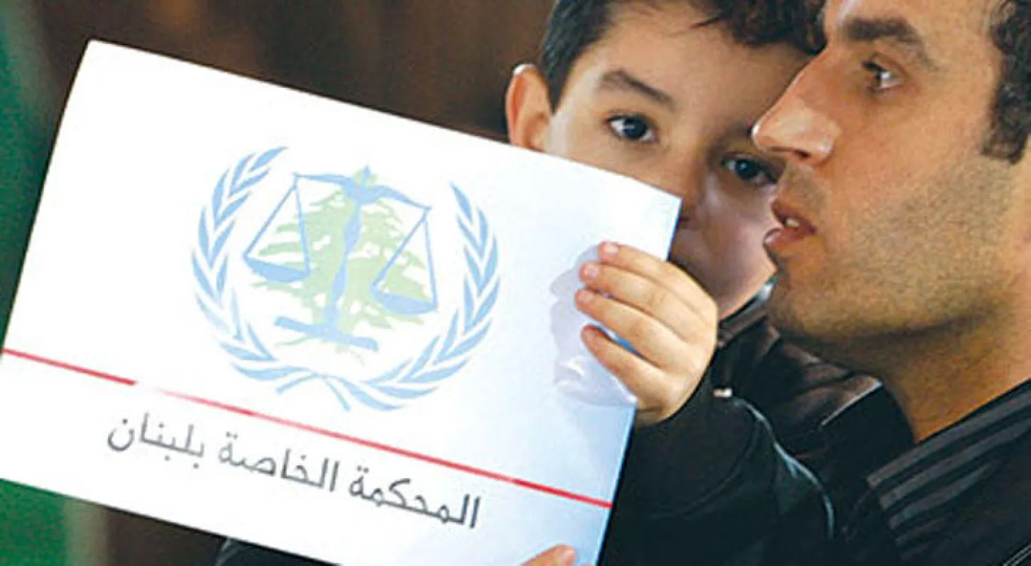 لبناني يحمل ابنه وبيده شعار المحكمة الدولية الخاصة بلبنان (رويترز)