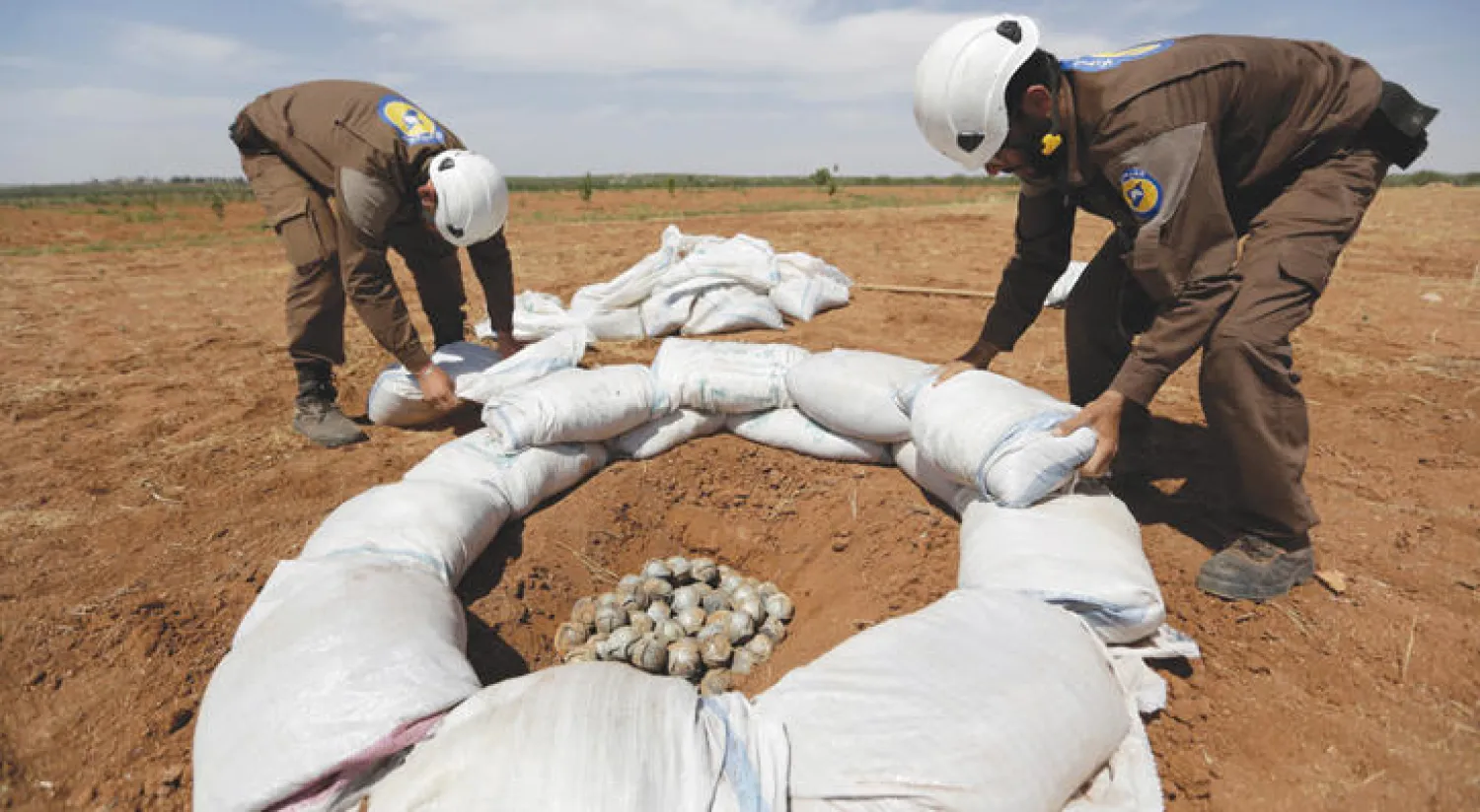 عناصر من الدفاع المدني السوري يجمعون بقايا شظايا قنبلة داخل حفرة بقرية التمانعة بريف ادلب اول من امس (رويترز)