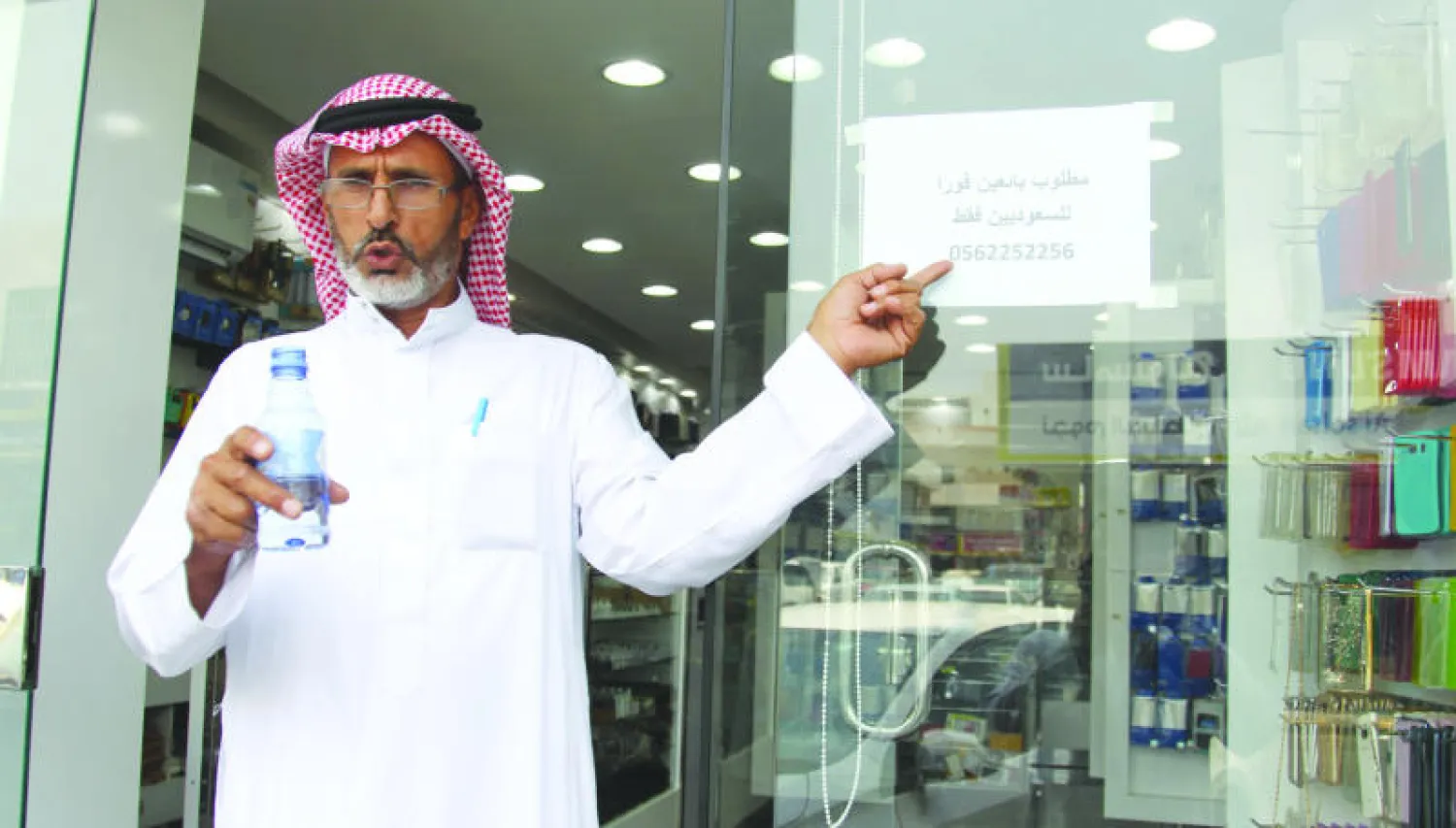 رجل يشير إلى إعلان بطلب سعوديين في أحد محال الاتصالات بجدة