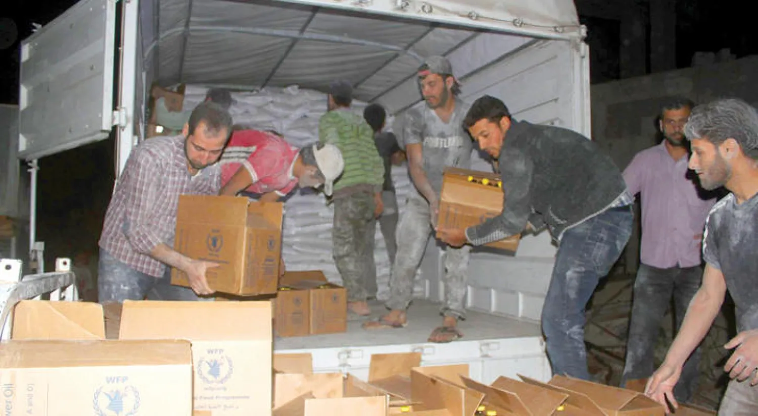 مواطنون سوريون يفرغون شاحنة محملة بالمساعدات في داريا (أ.ب)