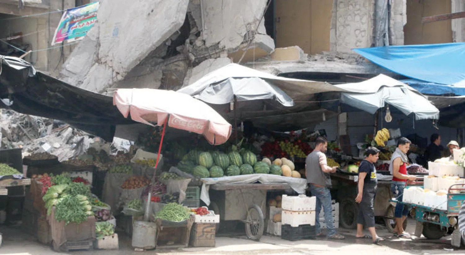 باعة في حي الشعار بحلب قبل موعد الإفطار أمس ينتظرون الزبائن تحت الأبنية المنهارة بفعل قصف الطيران الحربي للمنطقة (رويترز)