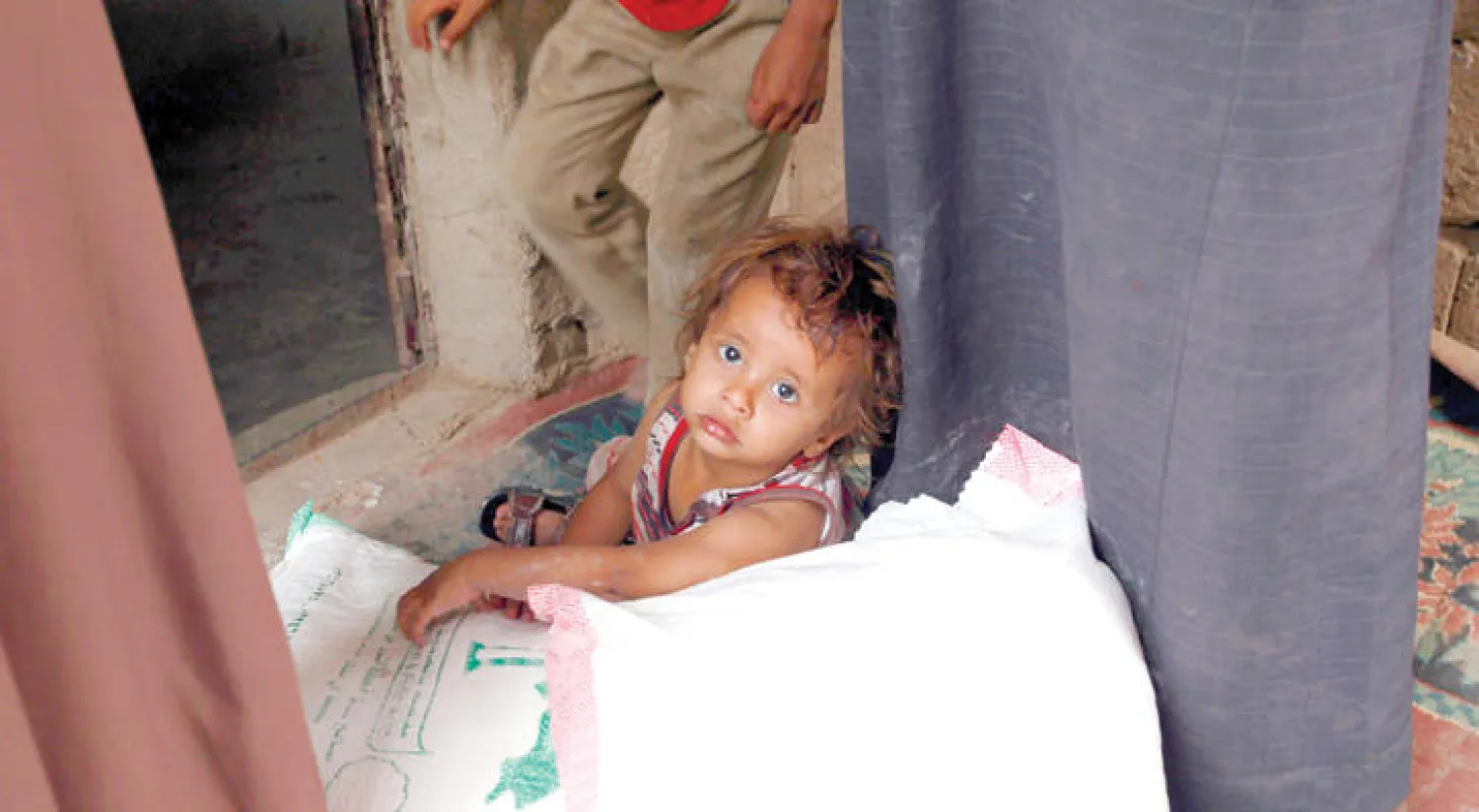 طفل يمني يجلس فوق أكياس المعونات الغذائية المقدمة من المنظمات الخيرية في صنعاء (أ.ف.ب)