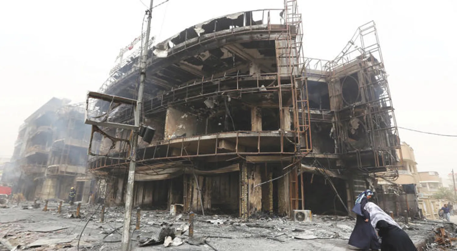 عراقيتان أمام مبنى دمره تفجير انتحاري في منطقة الكرادة وسط بغداد صباح أمس (أ.ف.ب)