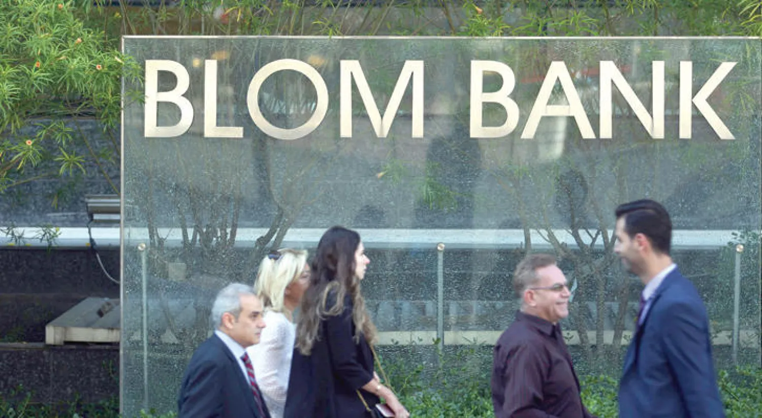 لبنانيون يعبرون مقر فرع بنك لبنان والمهجر (بنك بلوم) في العاصمة بيروت بعد وقوع أضرار بمبناه إثر تفجير سيارة قربه في 13 من الشهر الماضي (إ ف ب)