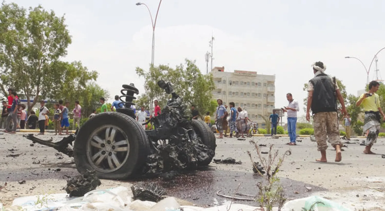 رجل أمن ومواطنون يتحلقون حول السيارة المفخخة بعد انفجارها في عدن أمس (رويترز)