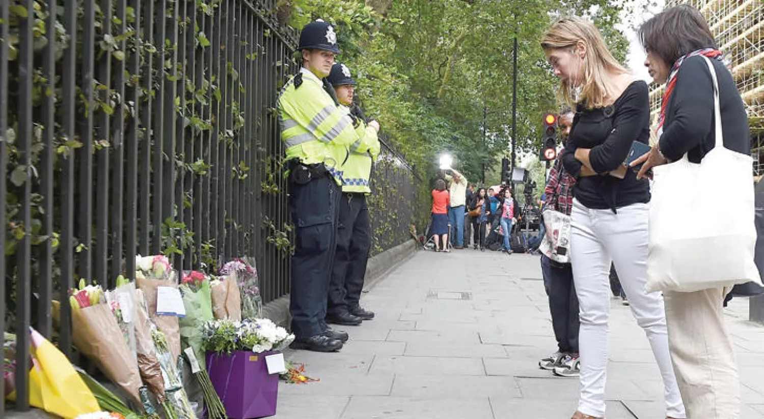 شرطيان من اسكوتلنديارد وأكاليل من الورود على أرواح الضحايا والمصابين بالقرب من موقع حادث الطعن في راسل سكوير بالعاصمة لندن أمس (إ.ب.أ)