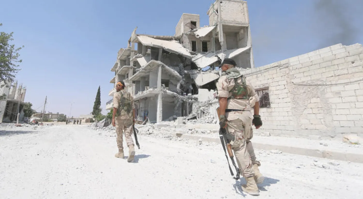 مقاتلان من «قوات سوريا الديمقراطية» في مدينة منبج بريف حلب قرب مبانٍ مدمرة تتصاعد منها الأدخنة بفعل المعارك مع تنظيم داعش (رويترز)