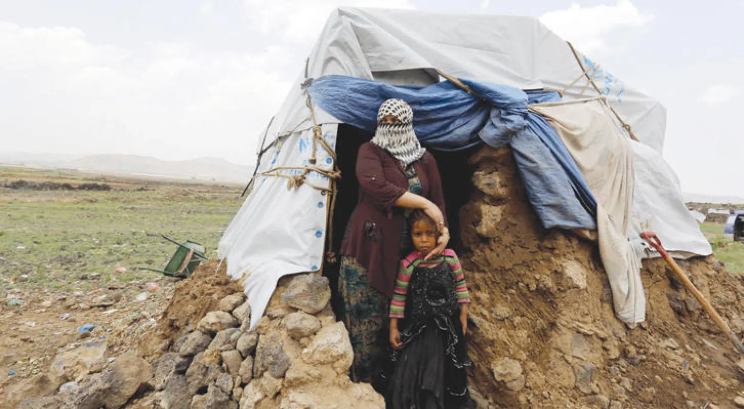 يمنية تطل مع طفلتها من خيمة بمخيم للنازخين في عمران شمال اليمن (إ.ب.أ)