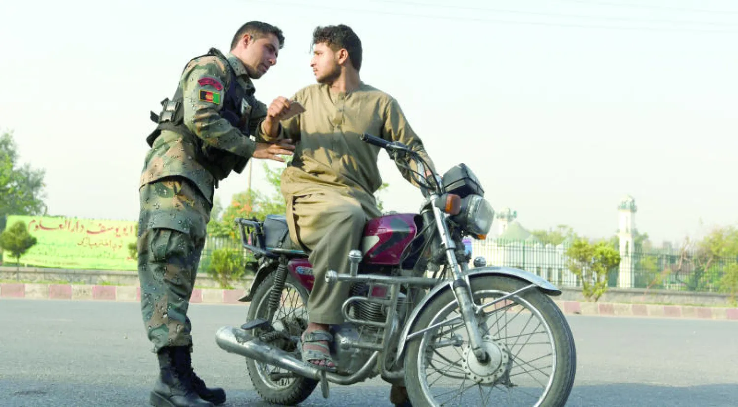 جندي أفغاني يفتش رجلاً على دراجة نارية في الطريق السريع خارج جلال آباد وسط تزايد في الإجراءات الأمنية قبل أيام من حلول عيد الأضحى المبارك (إ.ب.أ)