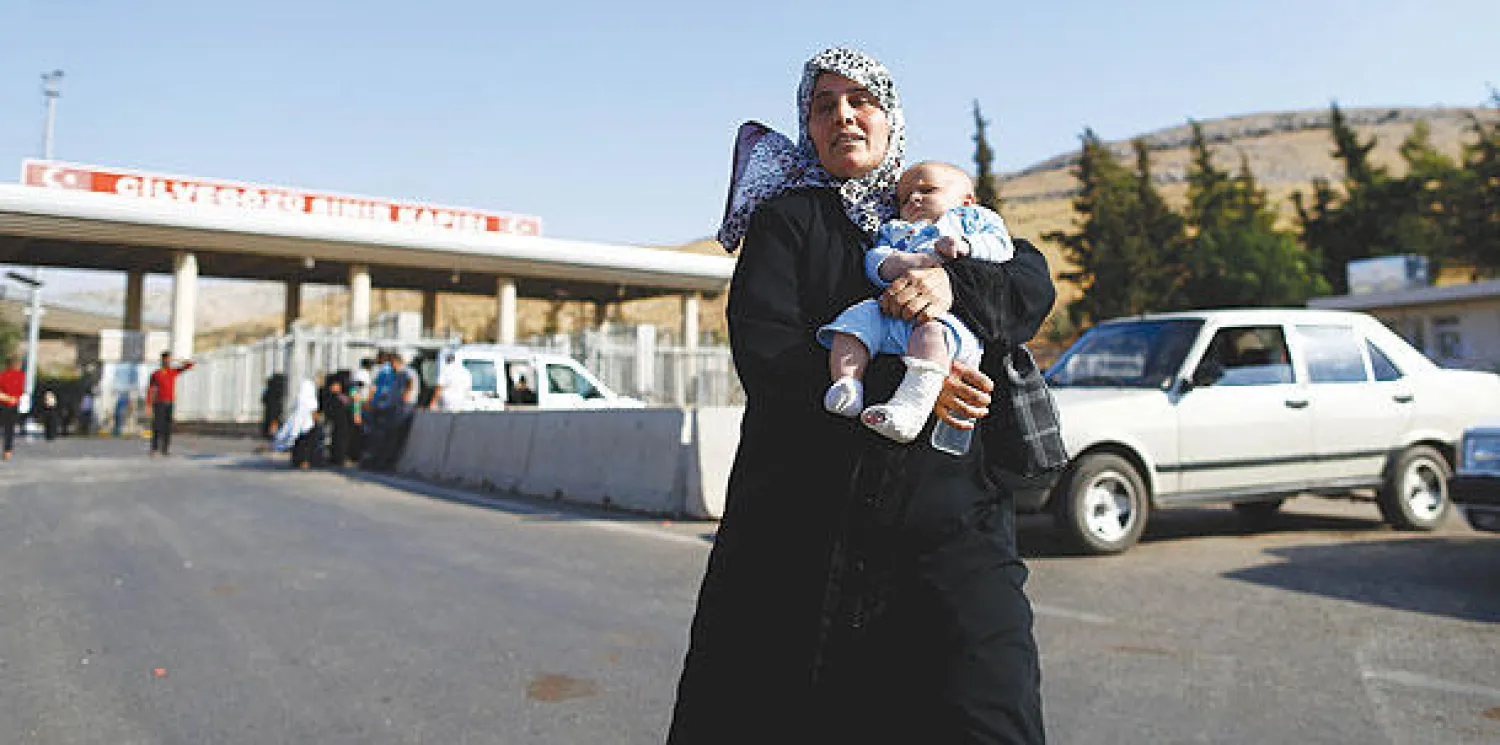سورية تحمل طفلها أثناء دخولها الأراضي التركية هربا من الصراع الدائر في سوريا (رويترز)