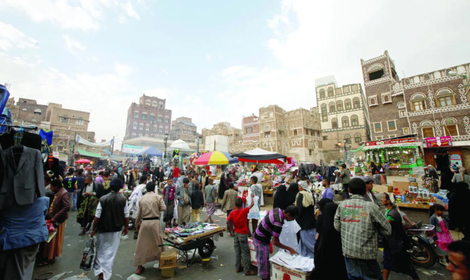 متسوقون يشترون بضائع من سوق شعبية تطل على المدينة القديمة في صنعاء (رويترز)