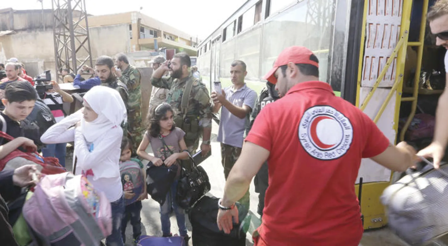 عناصر من الهلال الأحمر السوري يساعدون عائلات مقاتلي المعارضة في الصعود إلى إحدى الحافلات ضمن اتفاق لإخراجهم من حي الوعر أمس (أ.ف.ب)