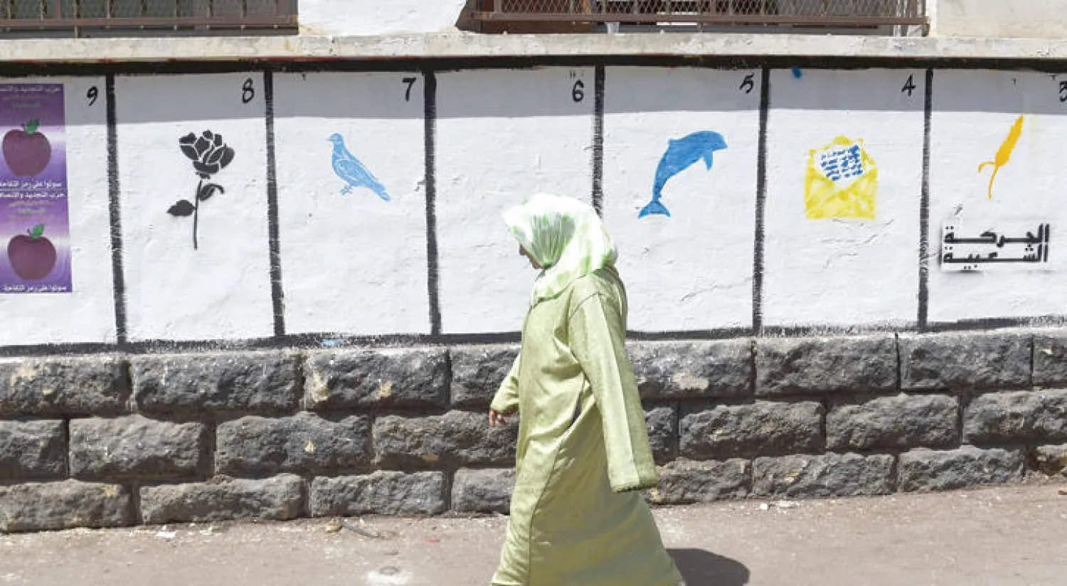 مغربية تمر من أمام حائط رسمت عليه رموز الأحزاب السياسية بعد انطلاق حملة الانتخابات (أ.ف.ب)