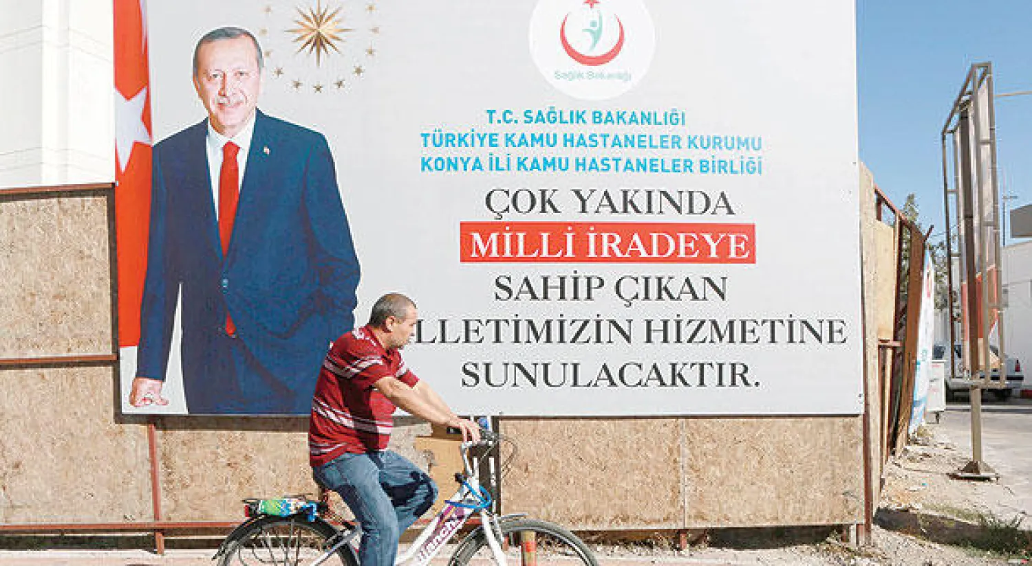 تركي راكباً دراجته يمر بجانب لوحة إعلانية لرئيس البلاد رجب طيب إردوغان في مدينة قونيا التي تؤيد نسبة كبيرة من سكانها حزب العدالة والتنمية (أ.ف.ب)