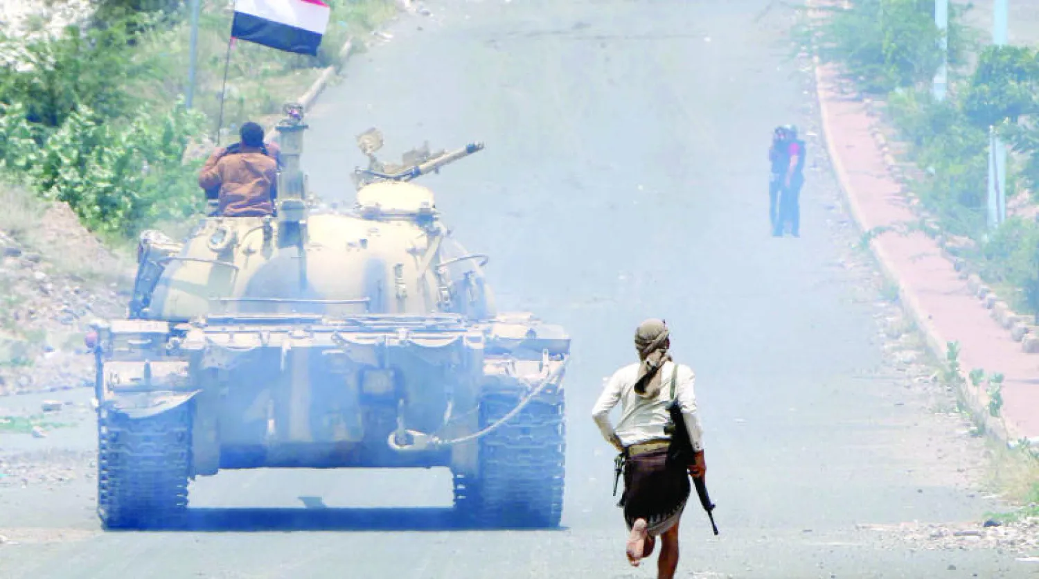 مقاتل موال للشرعية يجري خلف دبابة تحمل العلم اليمني في مدينة تعز (أ.ف.ب)