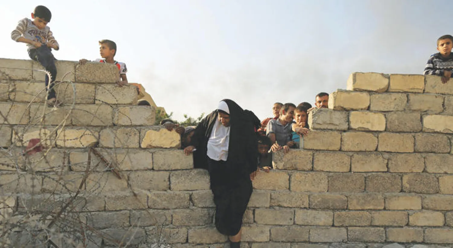 أمراة كبيرة في السن تحاول القفز فوق أحد الأسوار للتوجه إلى منطقة  القيارة جنوب الموصل هربا من الحرب الدائرة (رويترز)