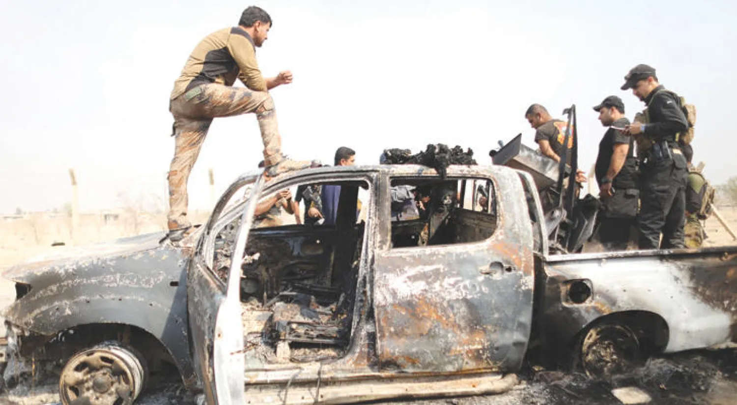 أفراد من القوات العراقية الخاصة يعاينون سيارة مدمرة لداعش في إحدى القرى القريبة من الموصل أمس ( رويترز)